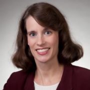 Susan, a white woman with dark brown hair, wears a white blouse and burgundy jacket.