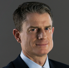Coleman, a white man with brown hair, wears a pale blue shirt, red tie and black jacket.