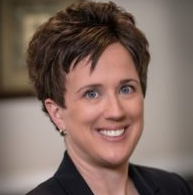 Jennifer, a white woman with brown hair in a pixie cut, wears a teal blouse and black jacket.