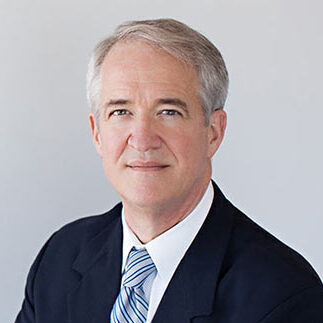 Jeff, a white man with grey hair, wears a white shirt, blue and white striped tie and black blazer.