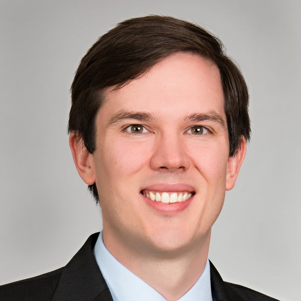 Erik, a white man with brown hair, wears a pale blue shirt and black jacket.