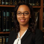 Sidney, a Black woman with black hair, wears a white blouse, black jacket and glasses.