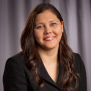 Erin, a woman with long brown hair, wears a black blouse and suit.