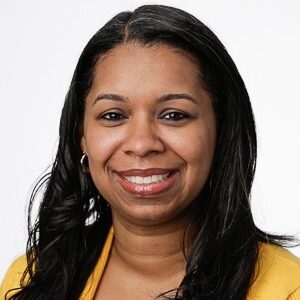 Giovanni Wade is a young woman with black hair and brown eyes. She is pictured smiling against a white background, and she is wearing a white shirt and a yellow blazer.
