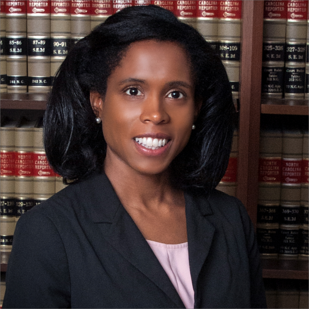 Nikki, a Black woman with black hair, wears a pale pink blouse and a black jacket.