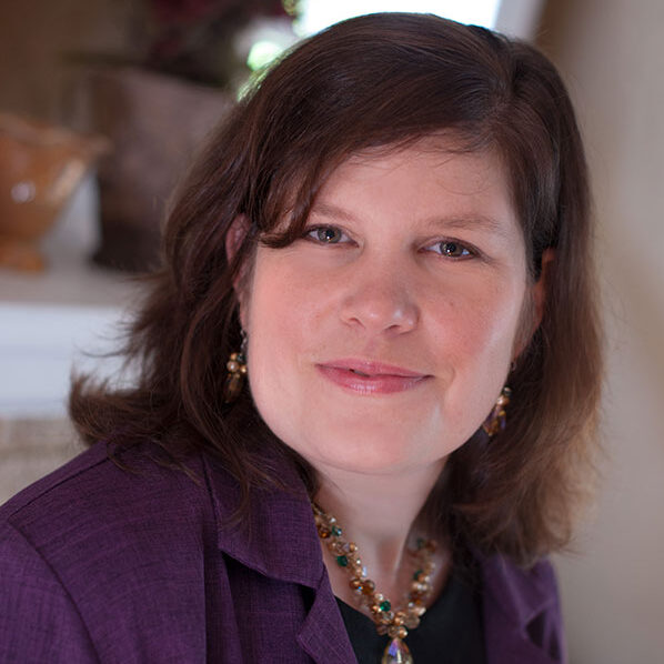 Lynna, a white woman with brown hair, wears a button-down dark purple shirt.