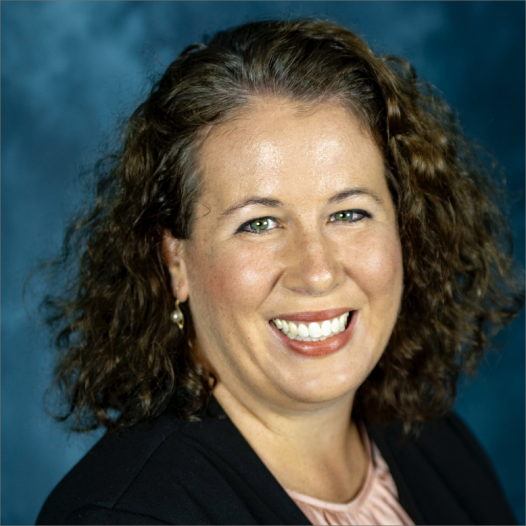 Casey, a white woman with curly dark brown hair, wears a pink blouse and black sweater.