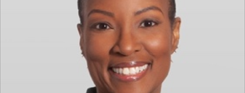 Cherell, a Black woman with black hair, wears a red blouse and black blazer, and she is smiling.