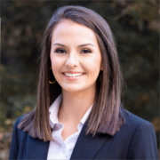 Zannah, a white woman with brown hair, wears a white shirt and black suit.