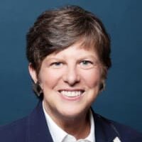 Barbara, a woman with short brown hair, wears a white button-down shirt and dark blue blazer.