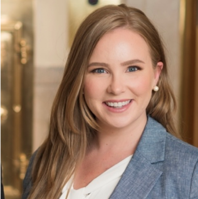Brooks, a white woman with long, light brown hair, wears a white shirt and light blue blazer.