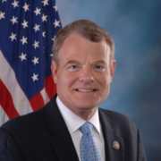 Mike, a white man with brown hair, wears a white shirt, blue tie, and black jacket.