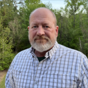 Mark Stewart, a white man with a grey beard, wears a white shirt with blue plaid.