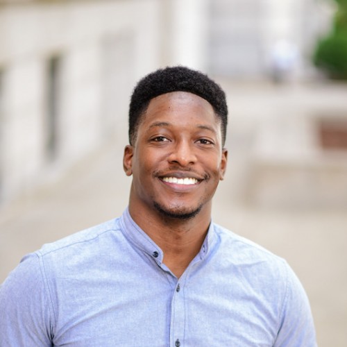 Peter, a Black man with black hair, wears a pale blue button-down shirt.