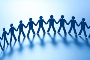 Silhouettes of people are shown in a line. The silhouettes are blue. The people are holding hands. 