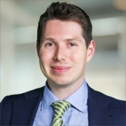 John, a white man with dark brown hair, wears a pale blue shirt, lime green and blue tie, and black suit. 