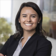 Clare, a white law student with shoulder-length brown hair, wears a grey button-down shirt, black jacket and pearl earrings.