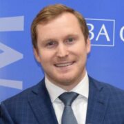 Bryan, a white man with red hair, wears a white shirt, blue tie and navy suit.