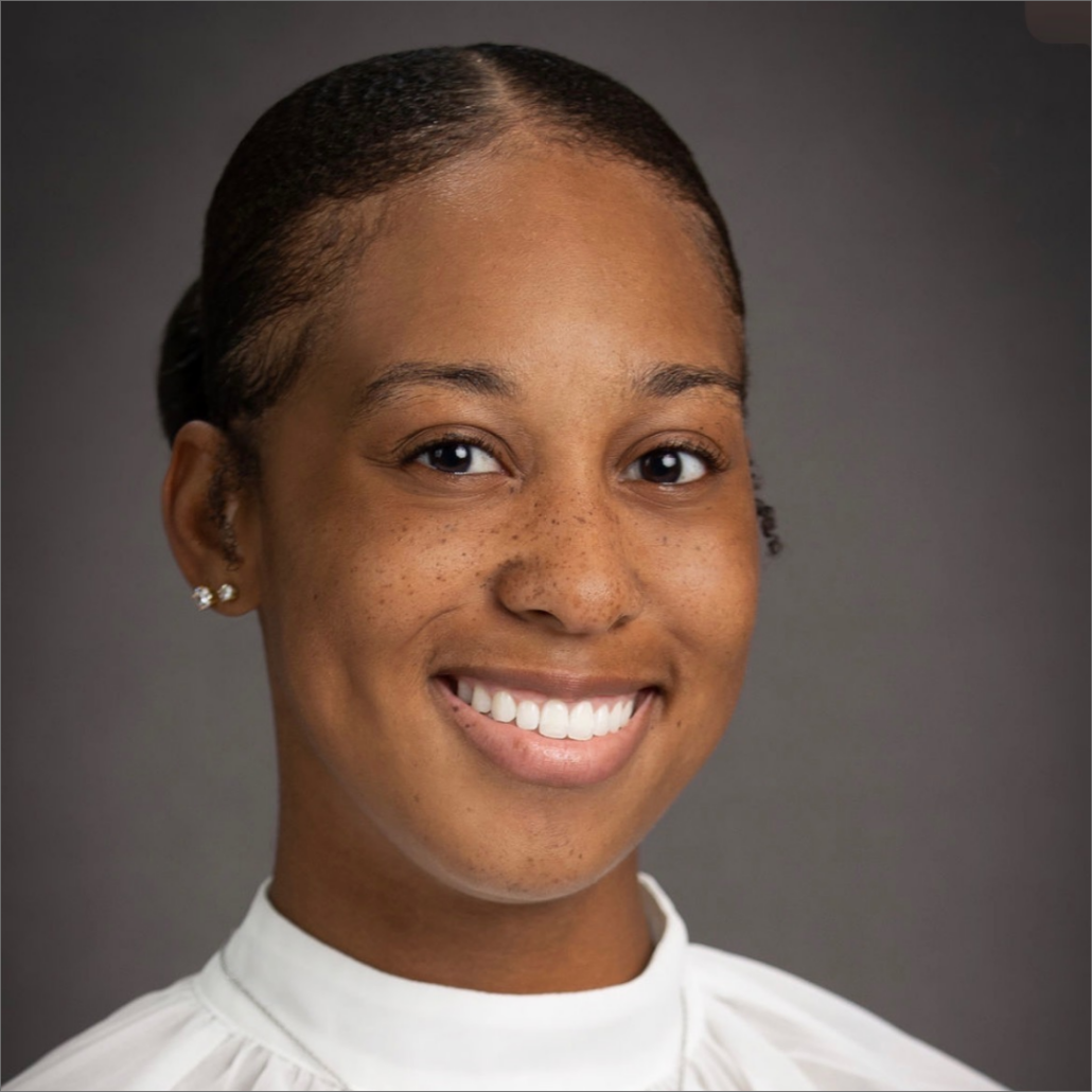 Robyn, a Black woman with black hair that is tied back, wears a white blouse.