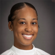 Robyn, a Black woman with black hair that is tied back, wears a white blouse. 