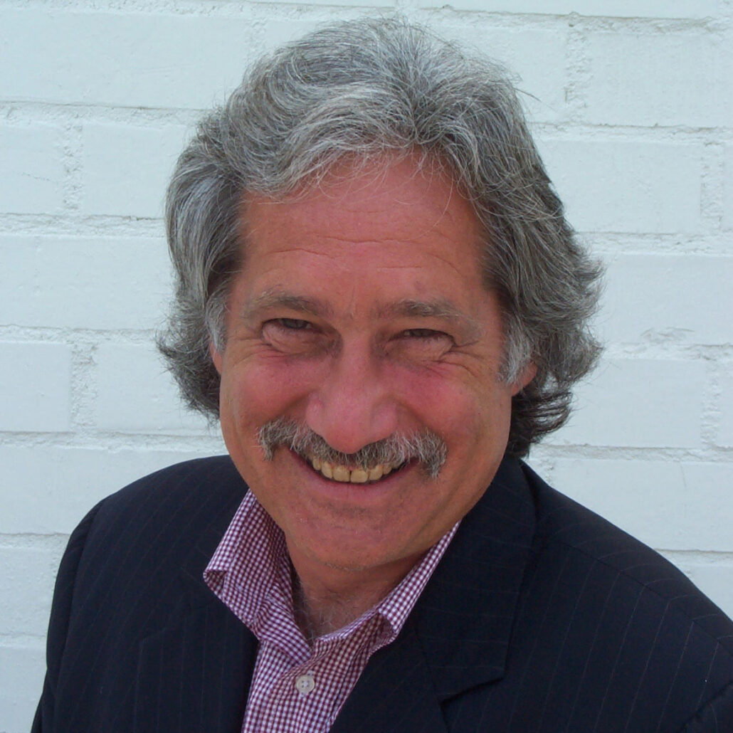 Harris, a white man with grey hair, wears a red and white checkered shirt and a black jacket.