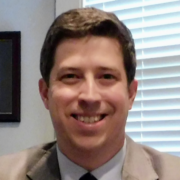 Brent, a white man with brown hair, wears a white shirt, dark tie, and tan suit. 