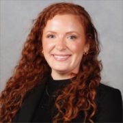 Abigail, a white woman with curly red hair, wears a black blouse.