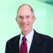 Jack Cummings, a white man with grey hair and wire-rimmed glasses, wears a pale blue shirt, red tie and black jacket.