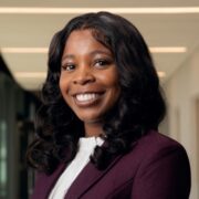 Maya, a Black woman with black hair, wears a white blouse and maroon blazer.