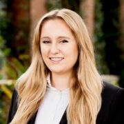 Savannah, a white woman with lon gblond hair, wears a pale grey blouse and a black jacket. 