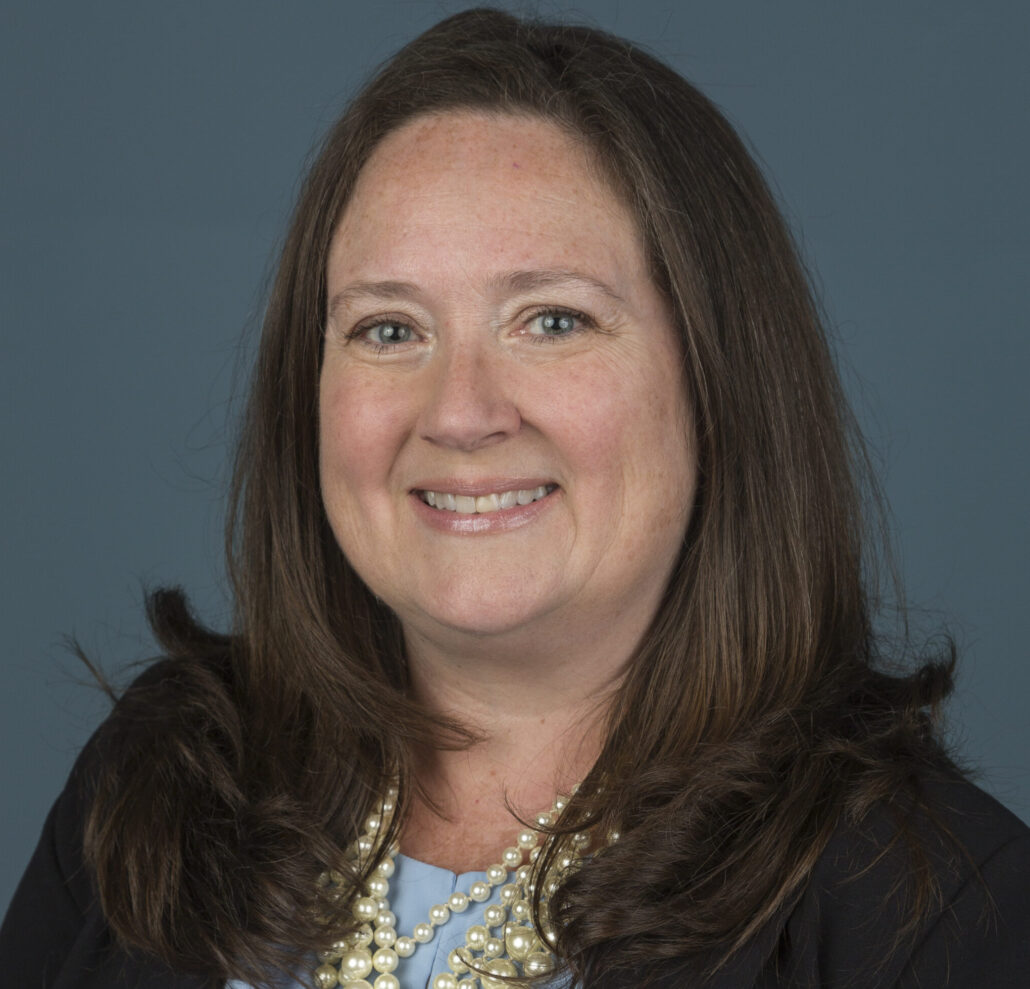 Karen, a white woman with dark brown hair, wears a pale blue shirt, a black blazer and a pearl necklace.