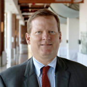 David, a white man with brown hair, wears a blue shirt, red tie and black jacket. 