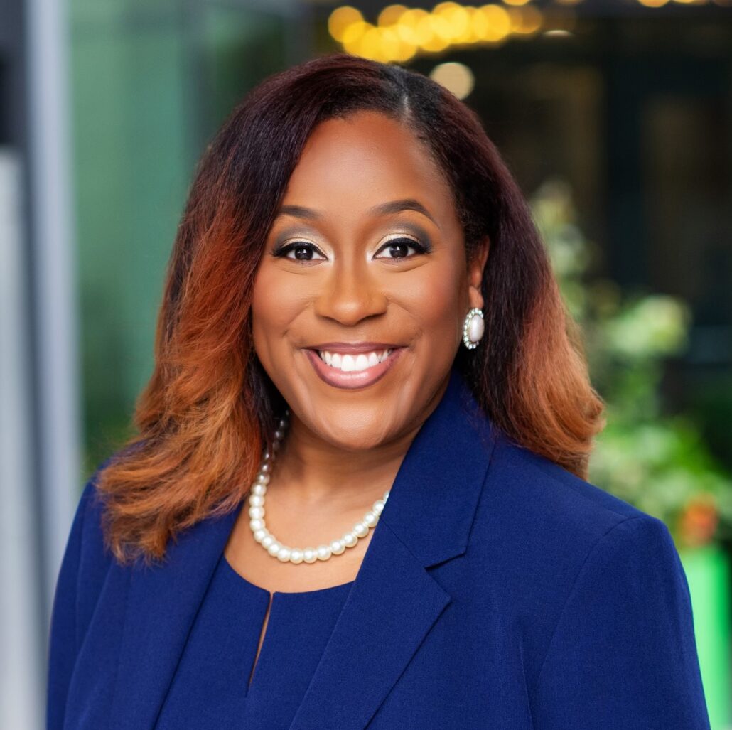 Chazle, a Black woman with black hair and auburn highlights, wears a blue suit and blazer and a pearl necklace.