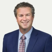 Rick, a white man with brown hair, wears a pale blue shirt, light purple tie, and navy suit.