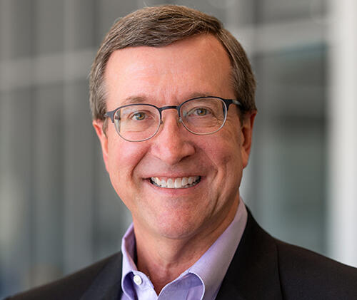 Eddie, a white man with brown hair and glasses, wears a light purple shirt and black jacket.