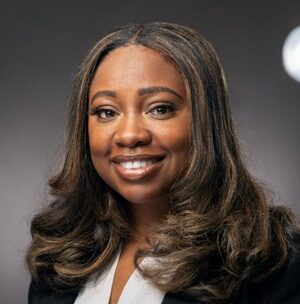 Tae, a Black woman with Black hair wears a white blouse and a black blazer.
