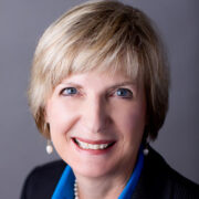 Ann, a white woman with blond hair, wears a blue blouse and black blazer.