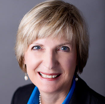 Ann, a white woman with blond hair, wears a blue blouse and black blazer.