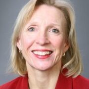 Denise, a white woman with blond hair, wears a red suit.