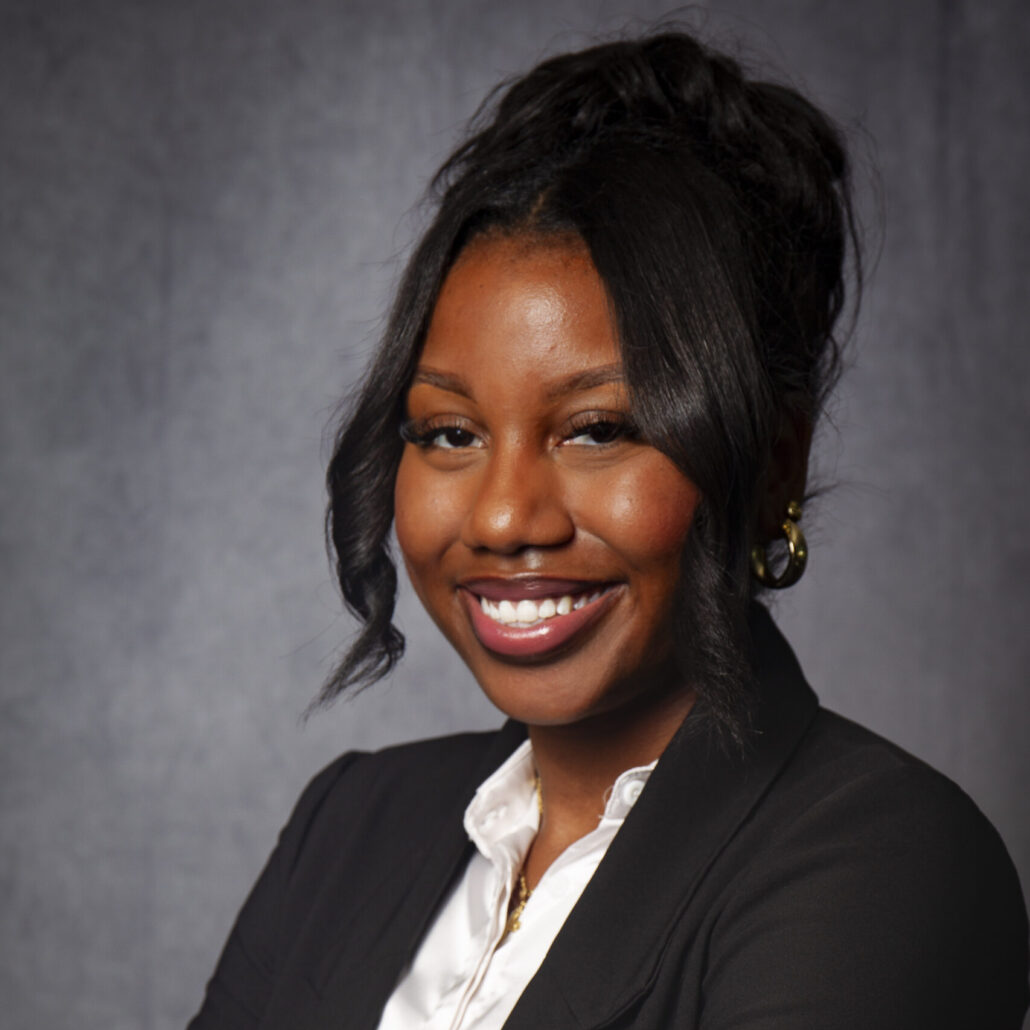 Tavaria, a Black woman with black hair, wears a white shirt and black blazer.