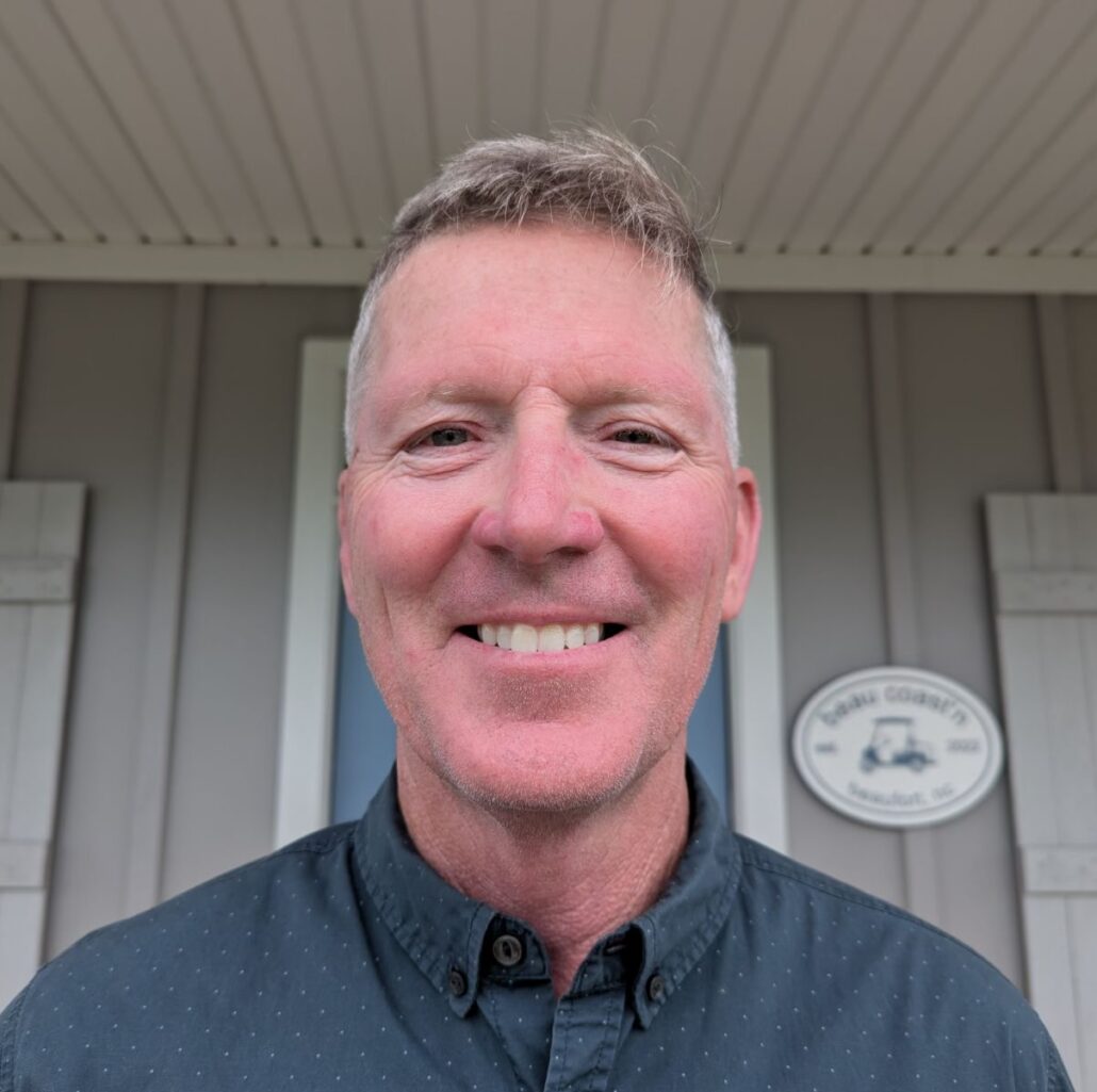 Don O'Toole is a white man with light brown hair. He is smiling, wearing a dark grey button-down shirt, and standing outside of a grey building.
