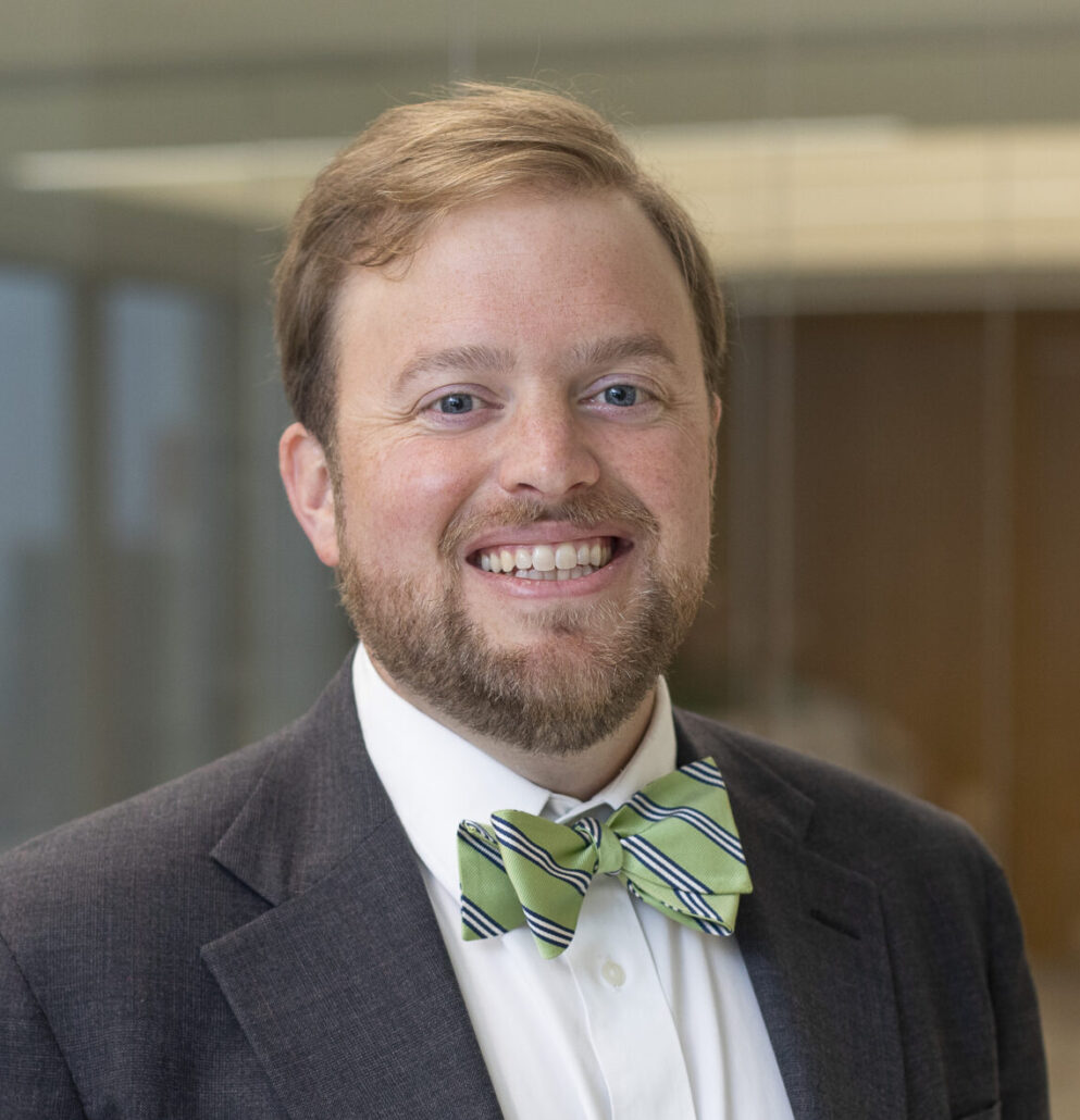 Will, a white man with light brown hair, wears a white shirt, pale green bowtie with darker green stripes, and a dark grey jacket.
