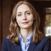 Sophia, a white woman with auburn hair, wears a pale blue shirt and a navy blazer.