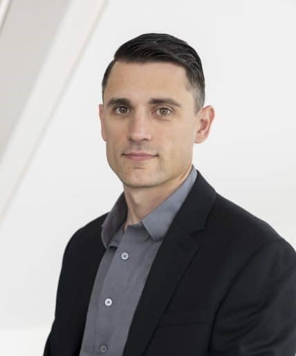 Todd, a white man with brown hair, wears a dark grey shirt and black blazer.