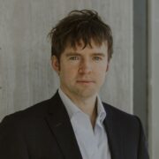 Brad, a white man with brown hair, wears a white shirt and black suit.