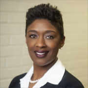 Afi, a Black woman with black hair, wears a white blouse, black jacket and pearl necklace.