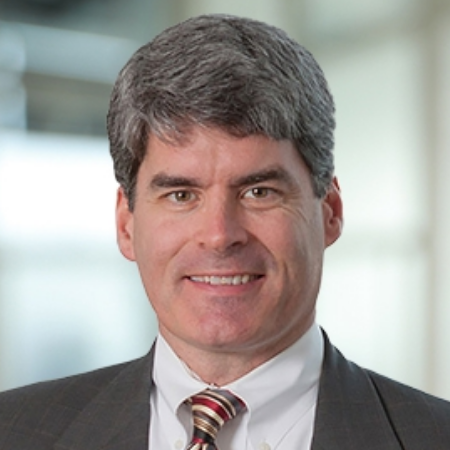 Erik, a white man with grey hair, wears a white shirt, red and white striped tie and grey blazer.