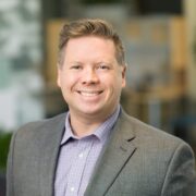 Jason, a white man with light brown hair, wears a light purple shirt and grey blazer. 
