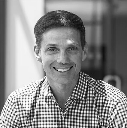 Paul, a white man with dark hair, wears a checkered shirt. The photograph is in black and white.