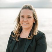 Bonnie, a white woman with blond hair, wears a black dress and dark grey blazer. 
